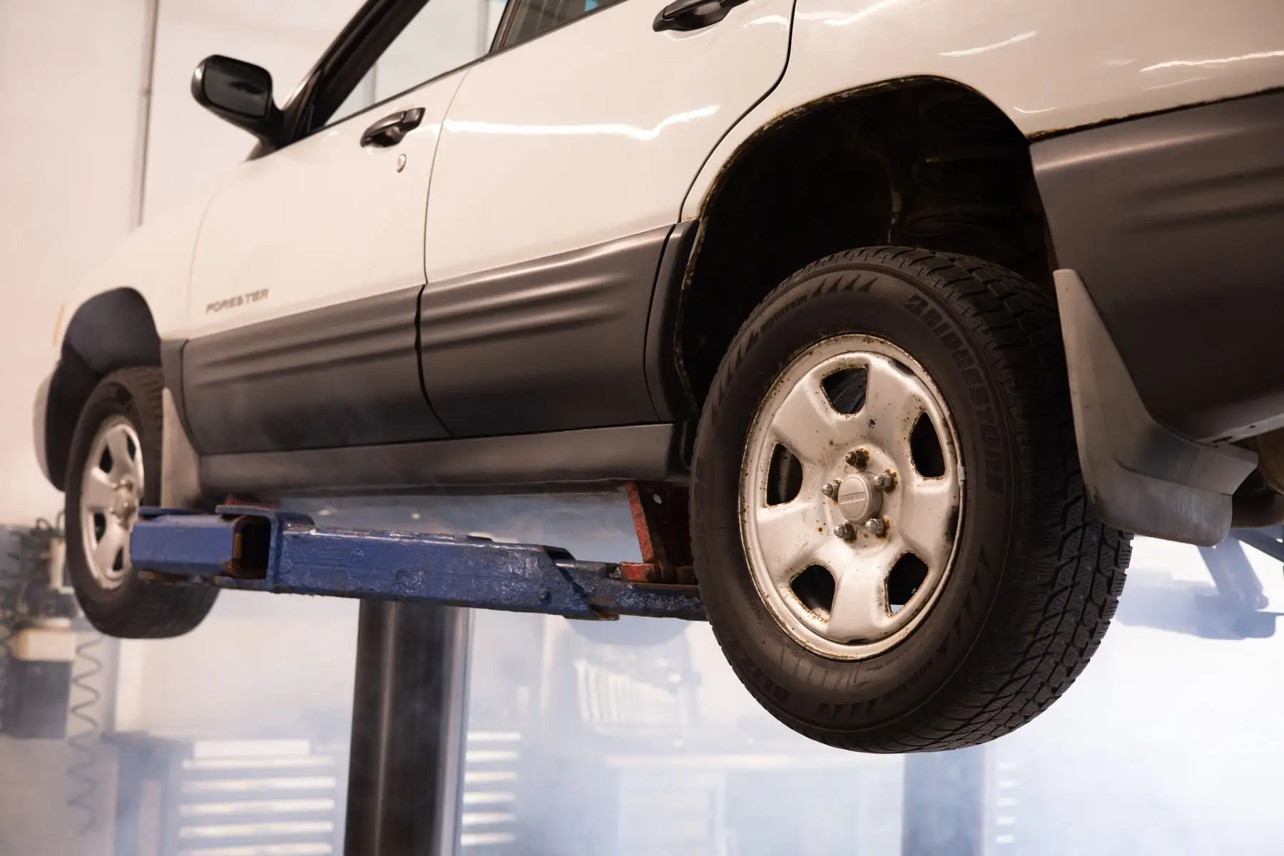 A car raised on a two post hoist inside a workshop, viewed from below the sill